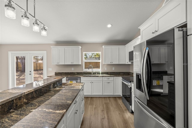 kitchen featuring sink, white cabinetry, hanging light fixtures, dark stone countertops, and stainless steel appliances