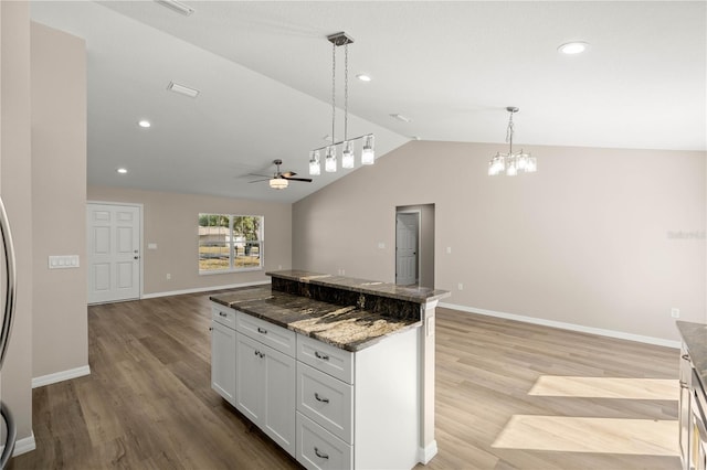 kitchen with lofted ceiling, decorative light fixtures, a kitchen island, dark stone counters, and white cabinets