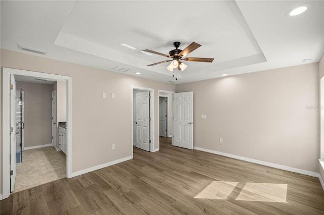 unfurnished bedroom featuring a raised ceiling, ceiling fan, and light hardwood / wood-style floors