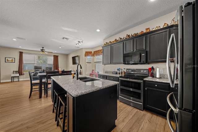 kitchen featuring appliances with stainless steel finishes, sink, a kitchen breakfast bar, a center island with sink, and light wood-type flooring