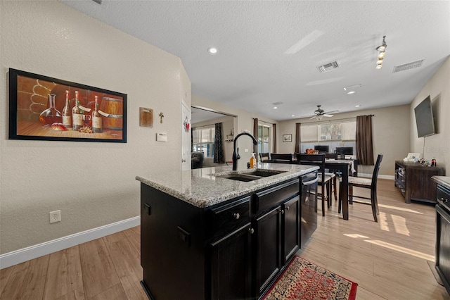 kitchen with an island with sink, sink, light stone counters, light hardwood / wood-style floors, and a textured ceiling