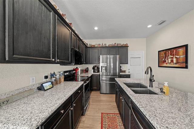 kitchen with appliances with stainless steel finishes, sink, light hardwood / wood-style floors, light stone countertops, and a textured ceiling