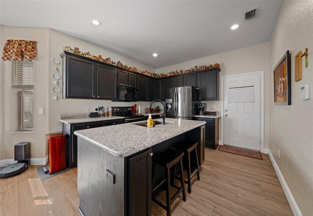 kitchen featuring stainless steel refrigerator with ice dispenser, sink, light wood-type flooring, range with electric stovetop, and a kitchen island with sink