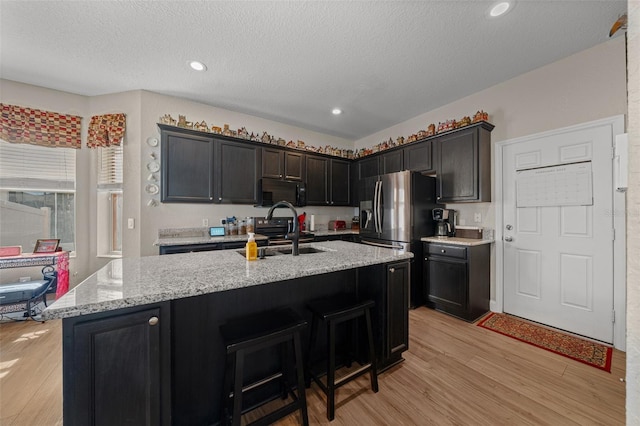 kitchen featuring sink, a kitchen island with sink, light stone counters, light hardwood / wood-style floors, and a textured ceiling