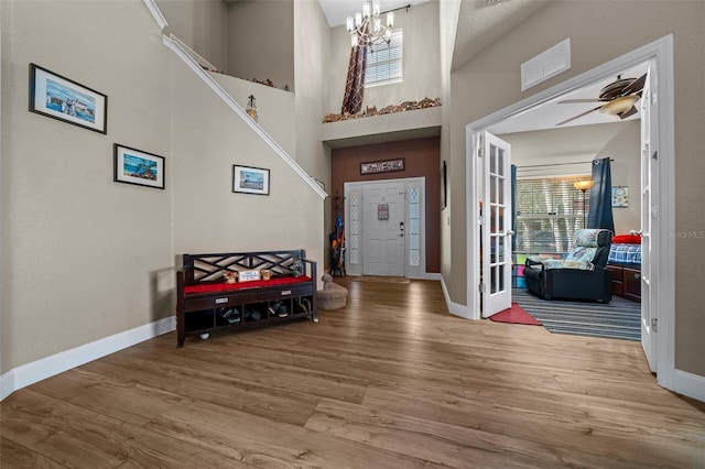 foyer entrance featuring hardwood / wood-style flooring, ceiling fan with notable chandelier, french doors, and a high ceiling