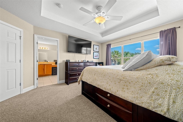 carpeted bedroom with ensuite bathroom, ceiling fan, a textured ceiling, and a tray ceiling