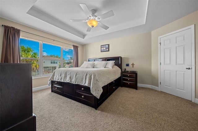 carpeted bedroom featuring a raised ceiling and ceiling fan