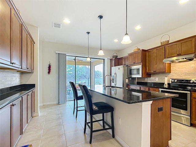 kitchen featuring pendant lighting, a breakfast bar, appliances with stainless steel finishes, backsplash, and a center island with sink