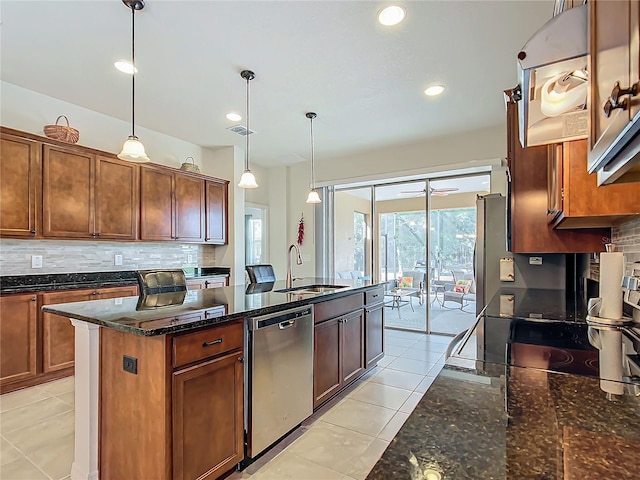 kitchen featuring sink, hanging light fixtures, stainless steel appliances, tasteful backsplash, and a center island with sink