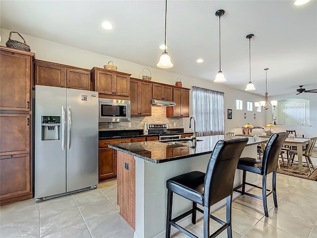 kitchen with pendant lighting, a center island with sink, stainless steel appliances, tasteful backsplash, and a kitchen bar