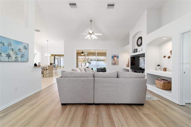 living room featuring ceiling fan with notable chandelier, light hardwood / wood-style flooring, and high vaulted ceiling