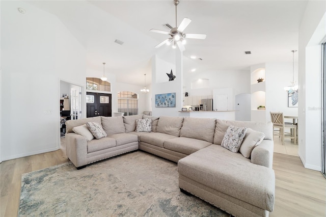 living room featuring ceiling fan with notable chandelier, high vaulted ceiling, and light wood-type flooring