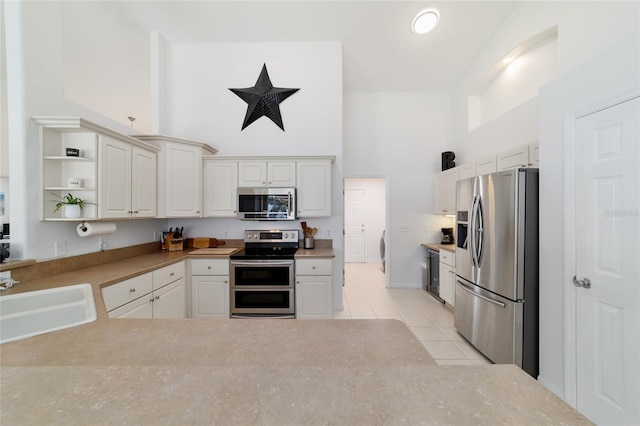 kitchen with white cabinetry, a towering ceiling, stainless steel appliances, and sink