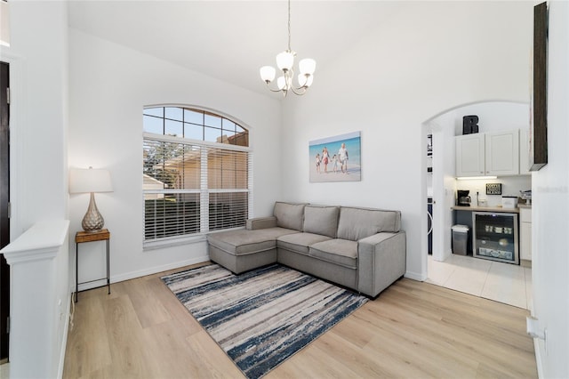 living room with wine cooler, light hardwood / wood-style flooring, high vaulted ceiling, and an inviting chandelier