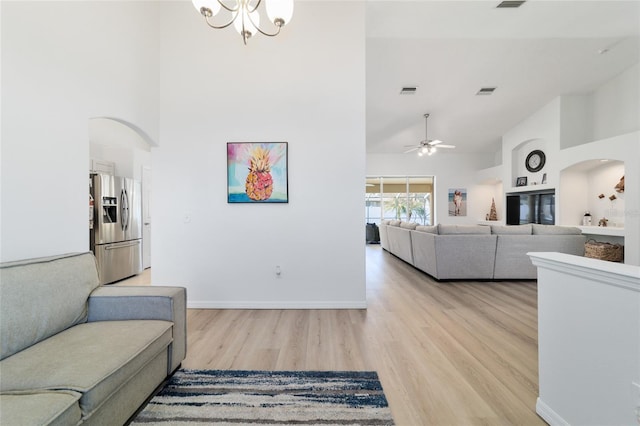 living room featuring ceiling fan with notable chandelier, high vaulted ceiling, and light hardwood / wood-style flooring