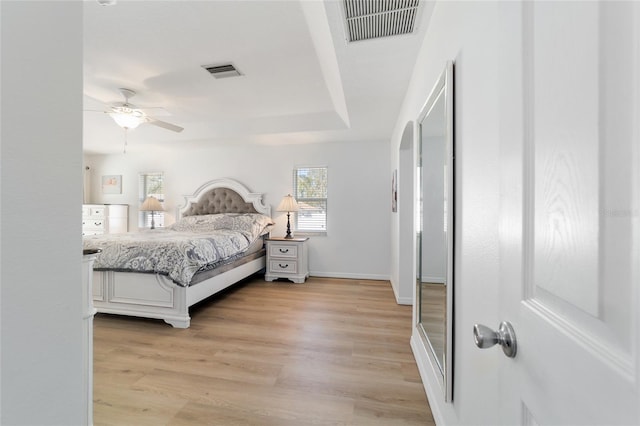 bedroom with ceiling fan, light hardwood / wood-style floors, and a tray ceiling