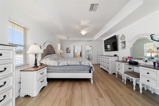 bedroom with ceiling fan, a raised ceiling, and light hardwood / wood-style flooring