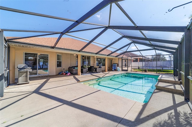 view of pool featuring grilling area, a patio, outdoor lounge area, and glass enclosure