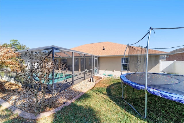 rear view of property with a trampoline, a lawn, and glass enclosure