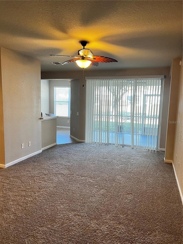 spare room with a textured wall, a ceiling fan, carpet flooring, a textured ceiling, and baseboards