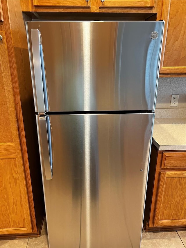 kitchen featuring light tile patterned floors, light countertops, brown cabinetry, and freestanding refrigerator