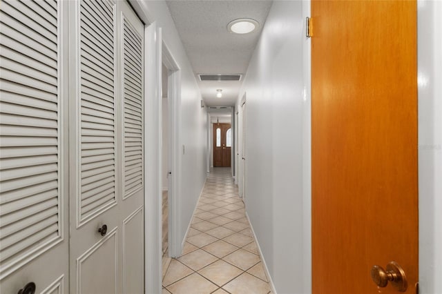 corridor featuring a textured ceiling and light tile patterned floors