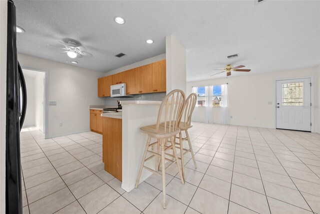 912 Chula Ct, Lady Lake, FL 32159 - kitchen with light tile patterned floors, black refrigerator, a kitchen breakfast bar, kitchen peninsula, and ceiling fan
