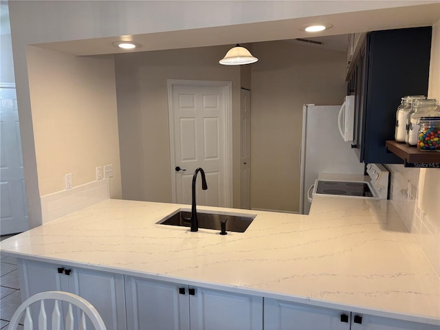 kitchen with decorative light fixtures, white microwave, white cabinetry, a sink, and range