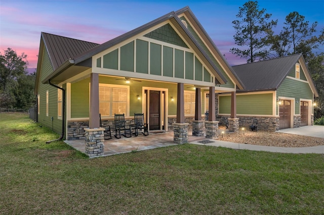 back house at dusk with a porch, a garage, and a yard