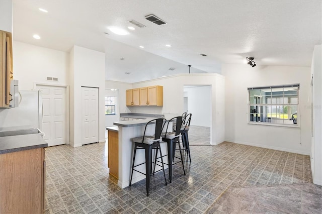 kitchen with a breakfast bar, visible vents, vaulted ceiling, and dark countertops