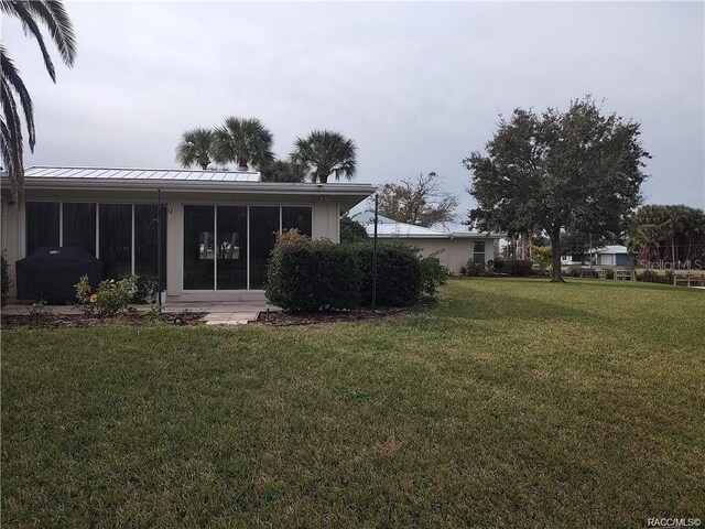 rear view of property featuring a sunroom, a yard, a standing seam roof, and metal roof