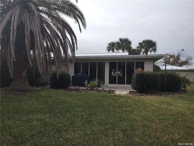 rear view of house with a sunroom, a yard, a standing seam roof, and metal roof