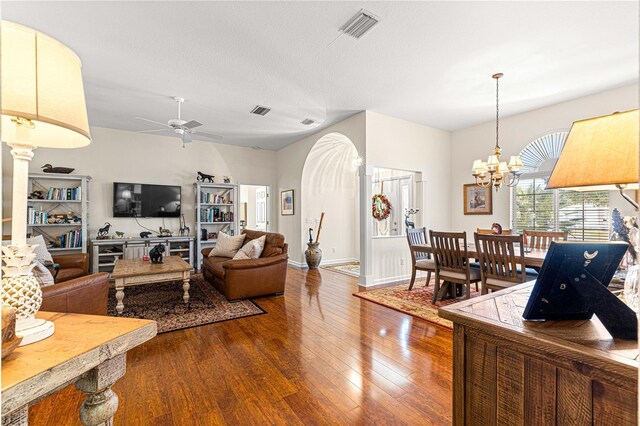 living room featuring wood-type flooring, ceiling fan with notable chandelier, and a textured ceiling