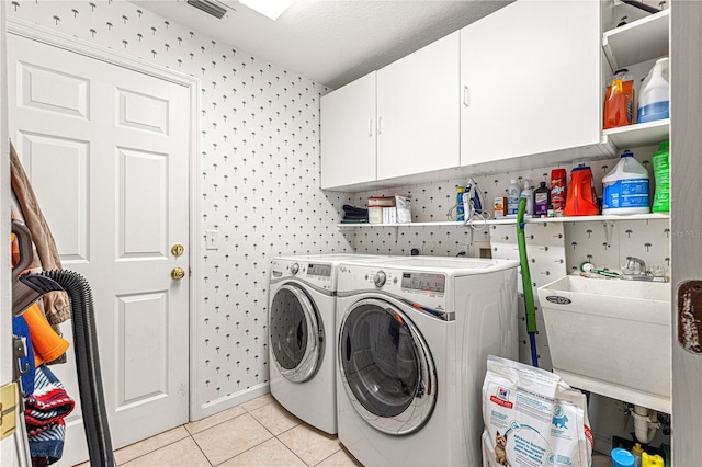 clothes washing area with washing machine and clothes dryer, sink, cabinets, a textured ceiling, and light tile patterned floors