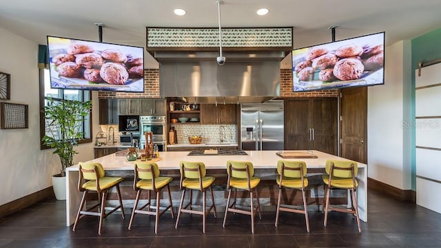 kitchen with a large island, dark brown cabinetry, stainless steel appliances, and a kitchen bar