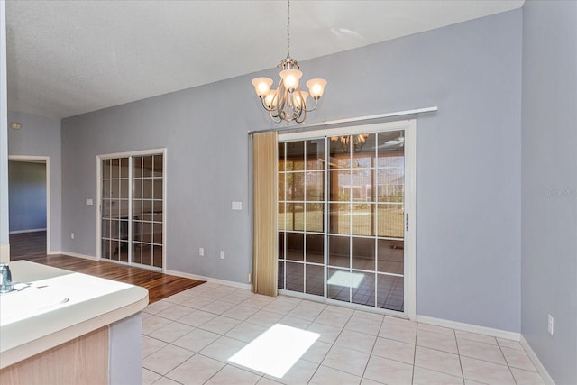 unfurnished dining area featuring a sink, a notable chandelier, baseboards, and light tile patterned floors