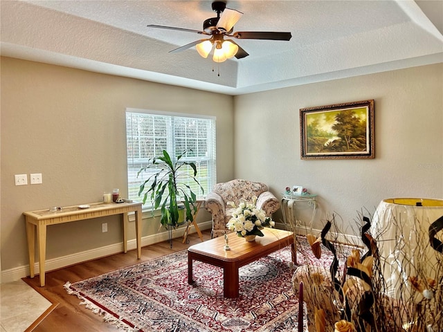 sitting room featuring ceiling fan, a tray ceiling, wood-type flooring, and a textured ceiling