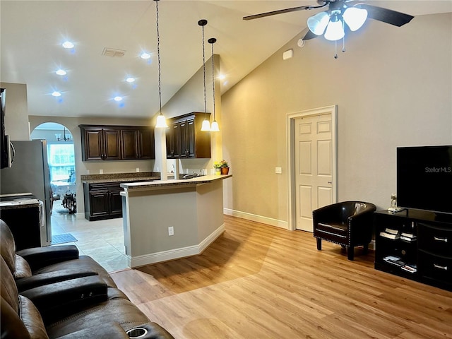 kitchen featuring stainless steel refrigerator, a kitchen bar, ceiling fan, dark brown cabinets, and light hardwood / wood-style flooring