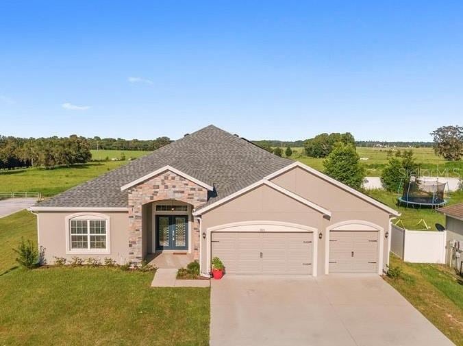 ranch-style house with a trampoline, a garage, and a front yard