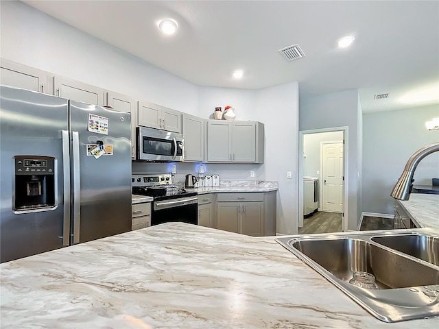 kitchen featuring visible vents, washer / clothes dryer, gray cabinets, stainless steel appliances, and a sink