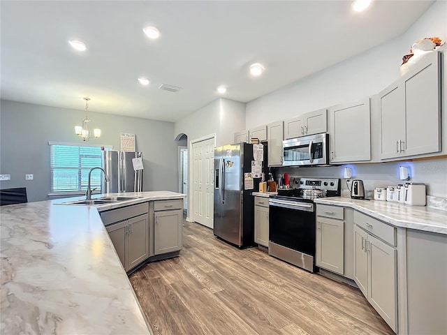 kitchen featuring stainless steel appliances, a sink, light wood-style floors, gray cabinets, and decorative light fixtures