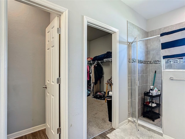 full bath with a stall shower, baseboards, a walk in closet, and wood finished floors