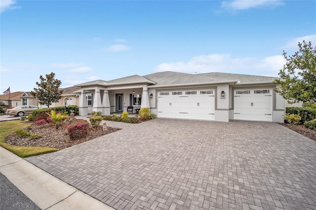 prairie-style home featuring a porch, decorative driveway, an attached garage, and stucco siding