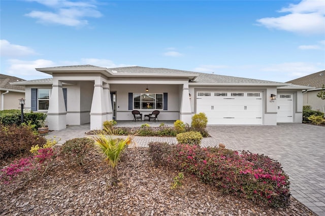 prairie-style home with a garage, covered porch, decorative driveway, and stucco siding