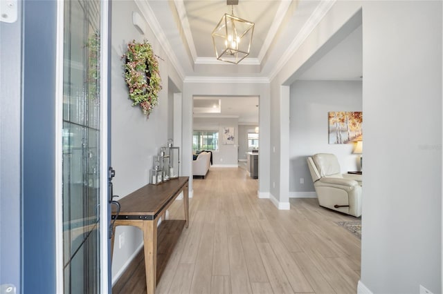 entryway with a tray ceiling, crown molding, light wood-style flooring, an inviting chandelier, and baseboards