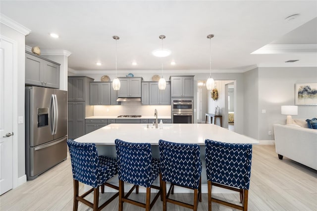 kitchen with a kitchen island with sink, stainless steel appliances, light countertops, gray cabinets, and decorative light fixtures