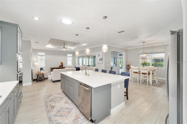 kitchen featuring a center island with sink, appliances with stainless steel finishes, open floor plan, gray cabinets, and light countertops