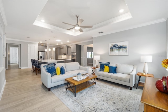 living area with light wood-style flooring, crown molding, a tray ceiling, and baseboards