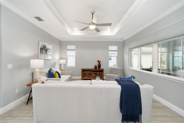 living area with baseboards, visible vents, ornamental molding, a tray ceiling, and light wood-style floors