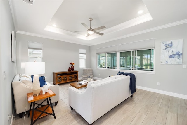 living area with light wood-style flooring, crown molding, a tray ceiling, and baseboards